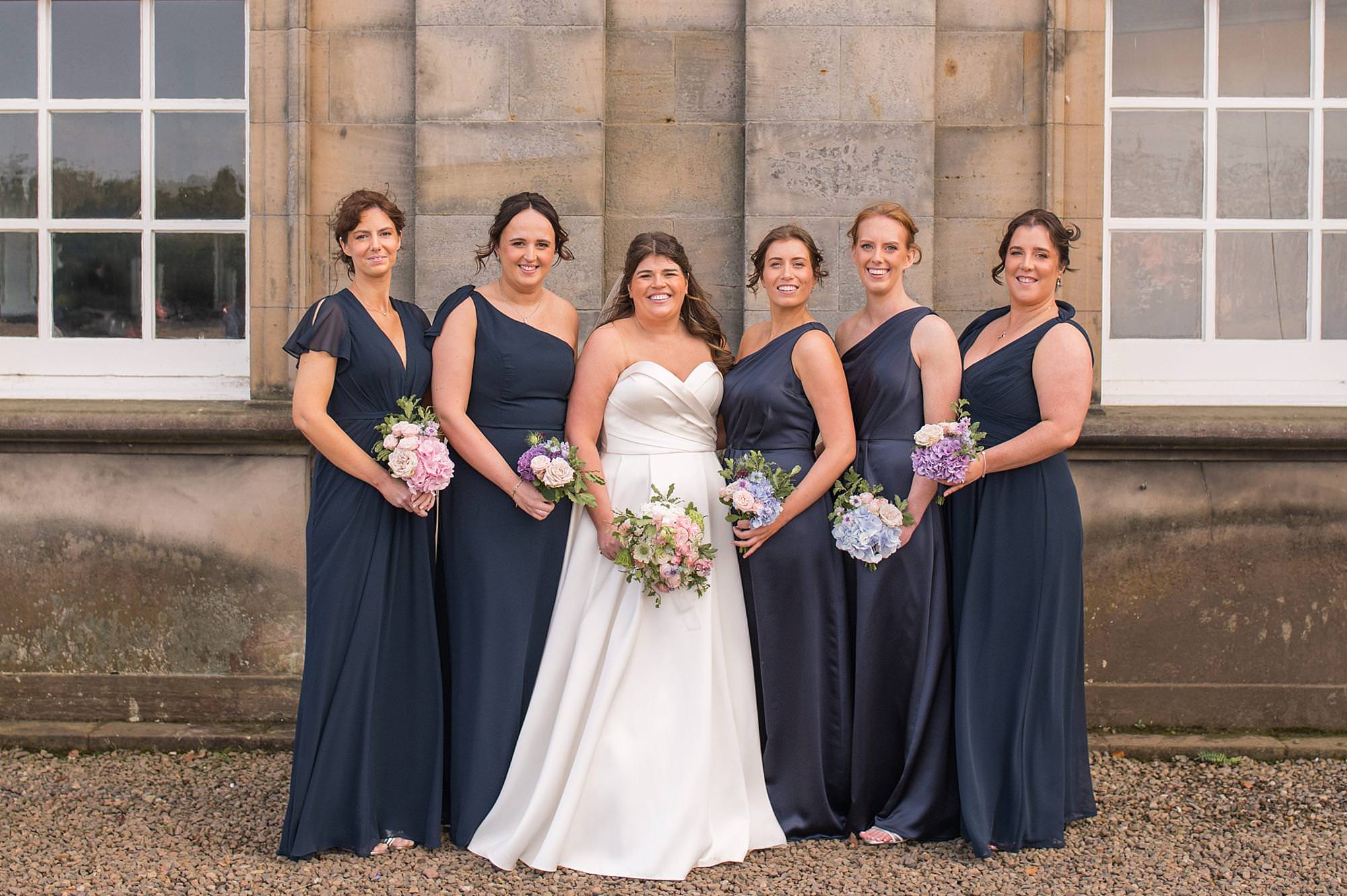 Bride and bridesmaids smile at came as they stand in a line at Hopetoun House