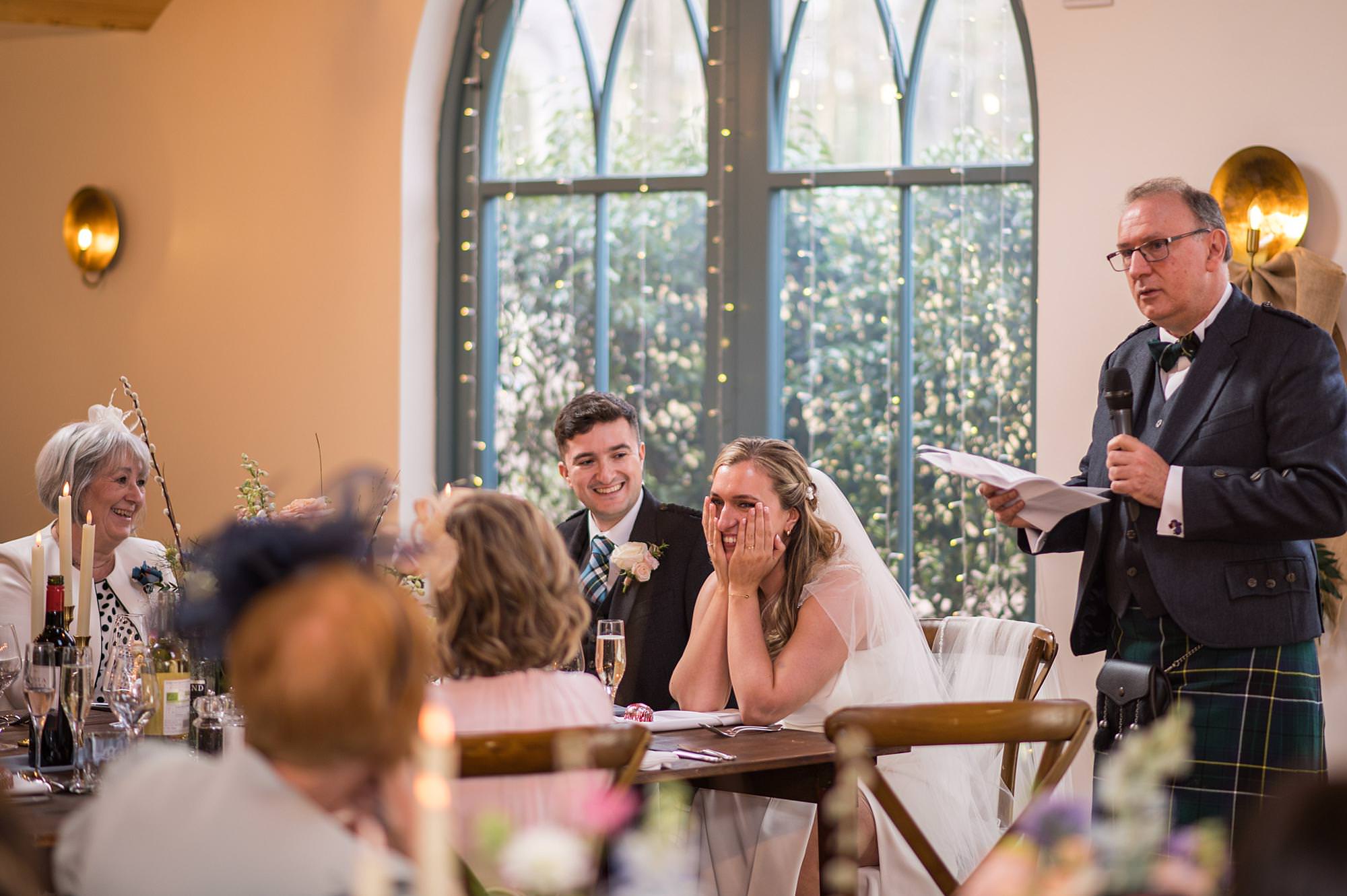 bride holds head in hands as she listens to her dad's speech